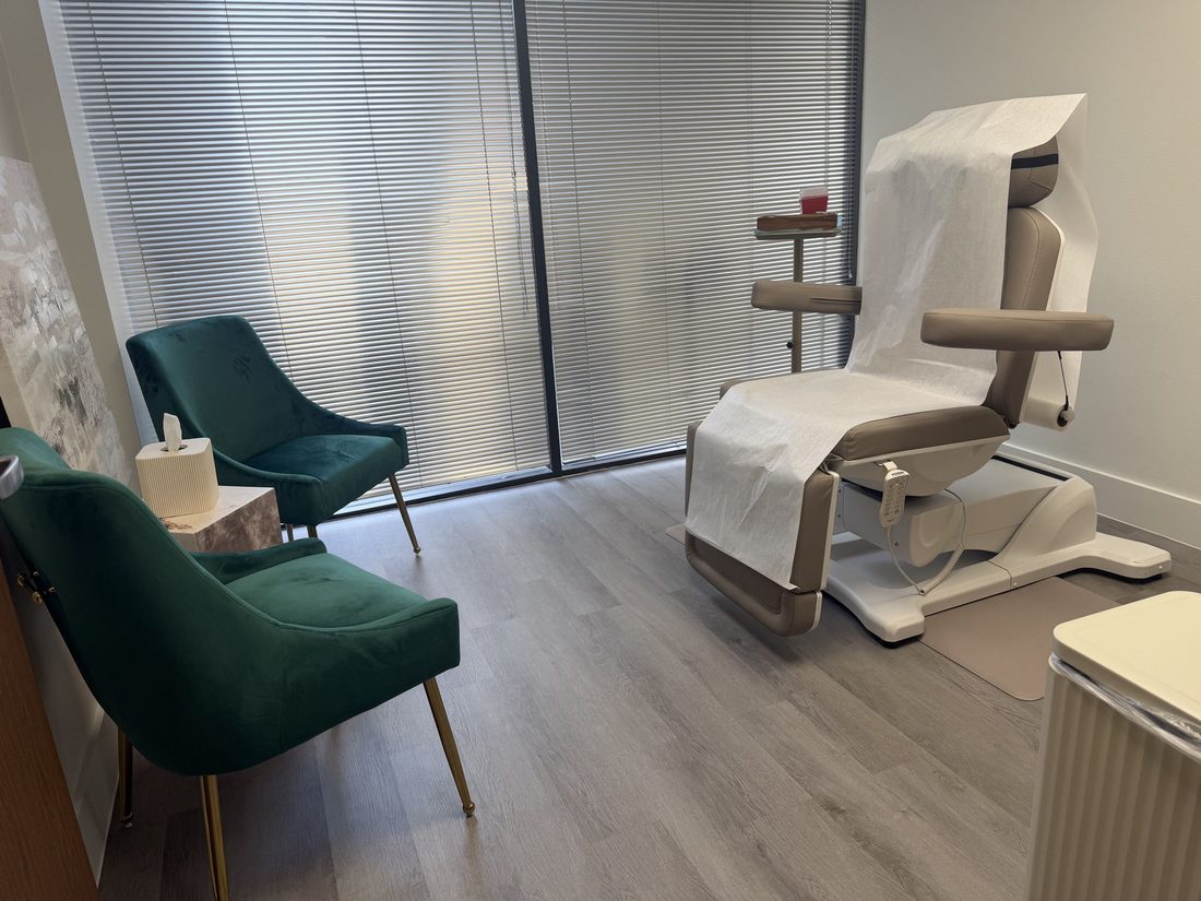 A treatment room at ZN Dermatology with a reclining treatment chair and green armchairs